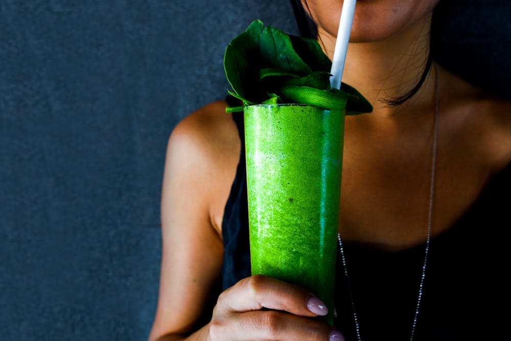 A woman in a black top drinking a green smoothie